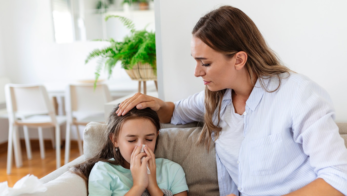 Woman comforting sick child who is blowing her nose into a tissue.