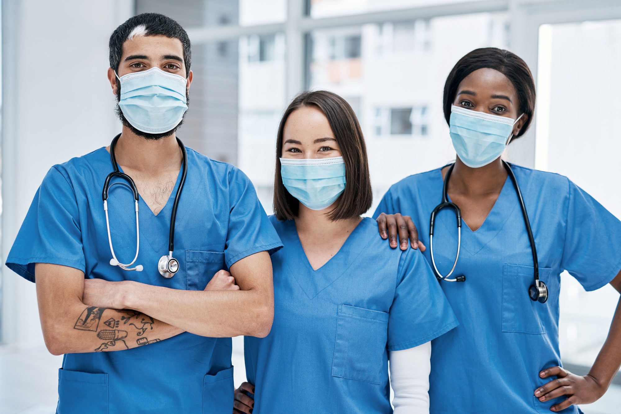 Three health care staff standing side by side wearing scrubs and masks