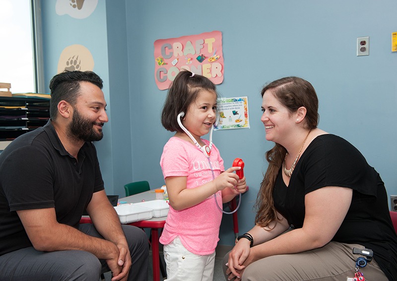 Young child at SHN Kids Care unit with her father and a child life specialist