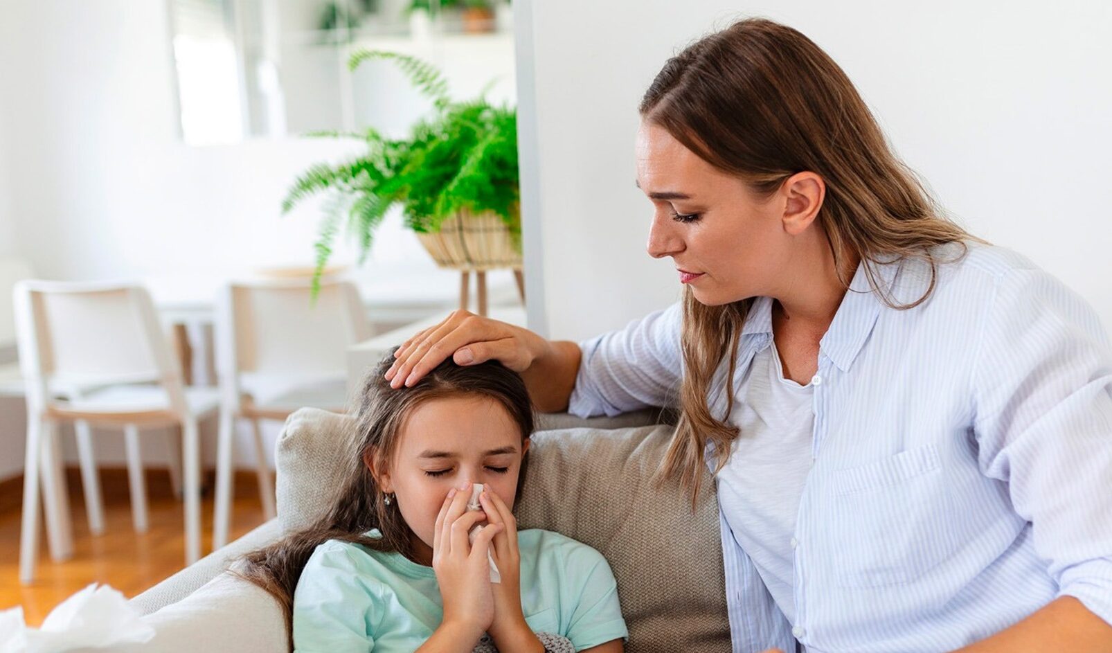 Woman comforting sick child who is blowing her nose into a tissue.